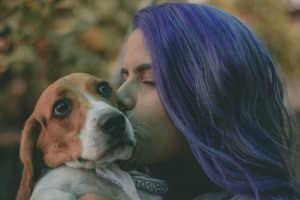  woman with purple hair kissing side of dogs face