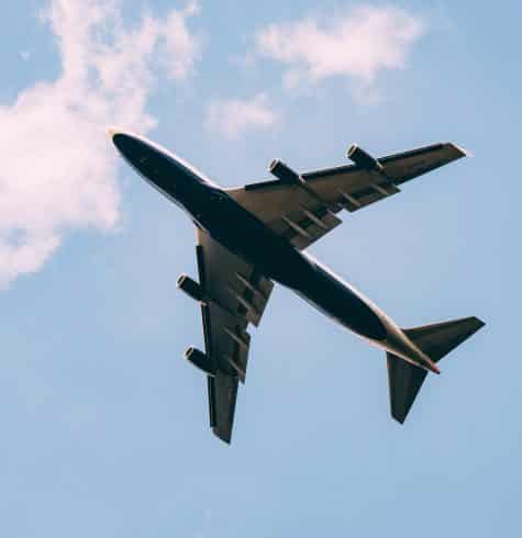 Picture of the underside of a plane flying through the sky with some clouds behind